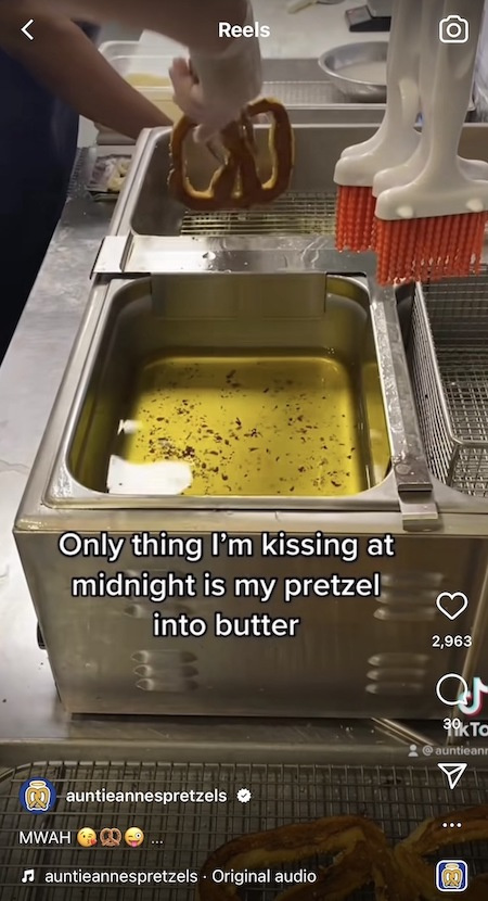   Μια θεία Άννα's Instagram Reel showing an Auntie Anne's pretzel maker dipping a pretzel into butter, and text on the screen that says Only thing I'm kissing at midnight is my pretzel into butter.