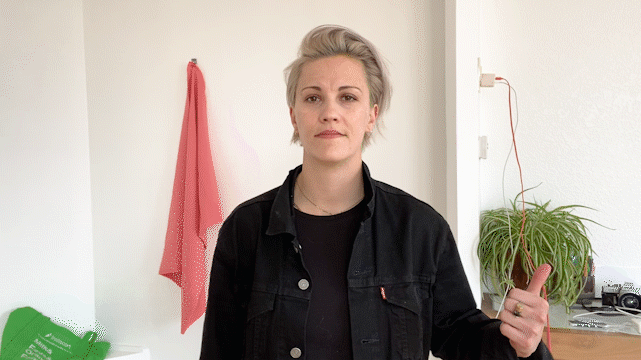 GIF-beschrijving: Videograaf wijst op afleidende items op hun achtergrond. Ze vegen over het camerascherm om een ​​opgeruimde achtergrond te onthullen.